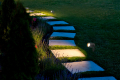 marble path of square tiles illuminated by a lantern glowing with a warm light in a backyard garden with a flower bed and a lawn copy space.